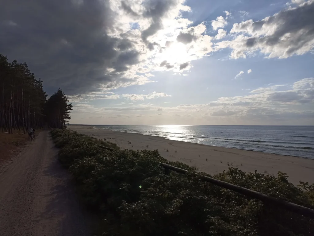 Zachód słońca nad Bałtykiem. Po lewej gruntowa ścieżka rowerowa i las. Po prawej plaża i Bałtyk.